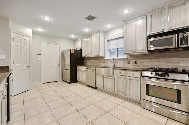 kitchen featuring stone counters, sink, decorative backsplash, light tile patterned floors, and appliances with stainless steel finishes