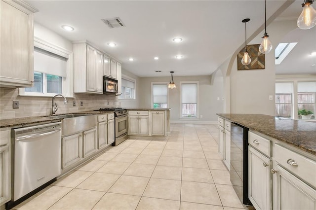 kitchen featuring a skylight, dark stone countertops, appliances with stainless steel finishes, tasteful backsplash, and decorative light fixtures