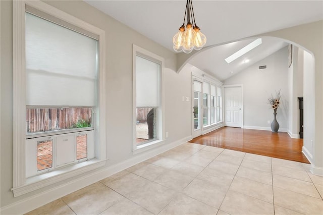 unfurnished dining area with lofted ceiling with skylight, light tile patterned floors, and a chandelier