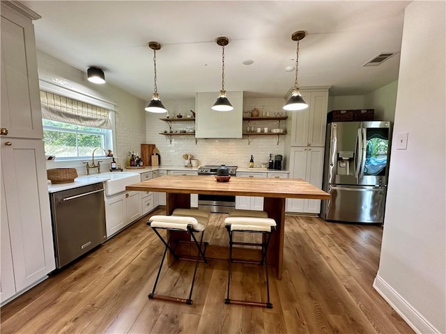 kitchen featuring appliances with stainless steel finishes, light wood-type flooring, sink, decorative light fixtures, and butcher block countertops