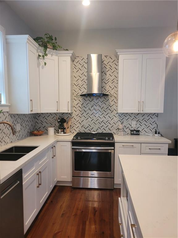 kitchen with white cabinets, stainless steel appliances, dark hardwood / wood-style floors, and wall chimney range hood