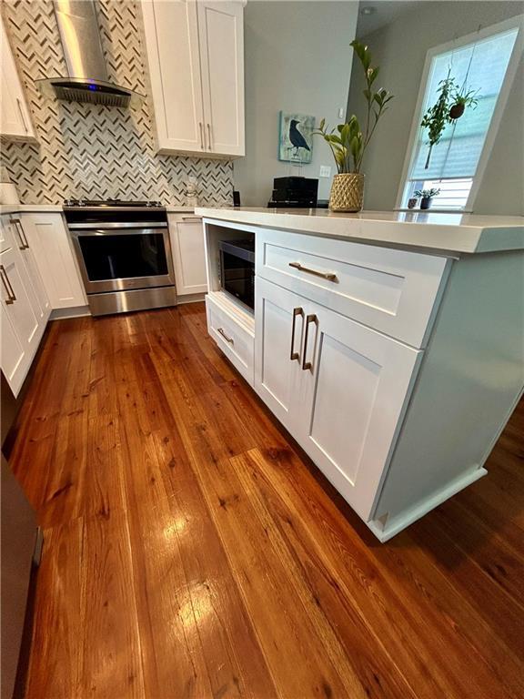 kitchen featuring white cabinetry, wall chimney exhaust hood, wood-type flooring, and appliances with stainless steel finishes