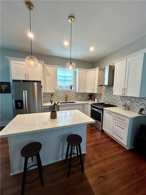 kitchen featuring wall chimney exhaust hood, stainless steel appliances, sink, decorative light fixtures, and a kitchen island