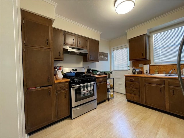 kitchen with stainless steel gas range oven, light hardwood / wood-style floors, decorative backsplash, dark brown cabinets, and ornamental molding