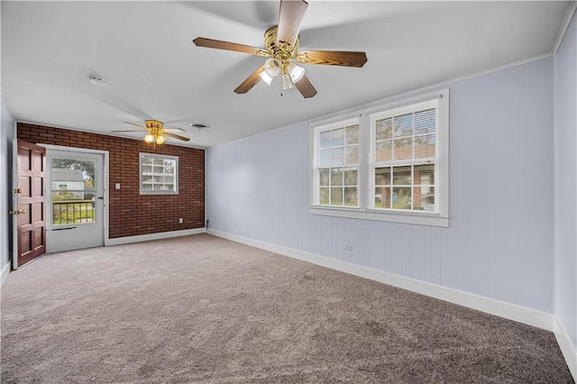 carpeted spare room featuring ceiling fan, brick wall, crown molding, and a wealth of natural light