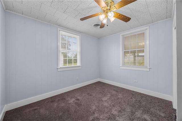 spare room with dark colored carpet, ceiling fan, and wooden walls