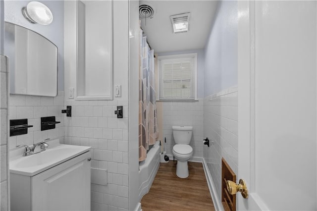 full bathroom featuring hardwood / wood-style flooring, shower / bath combination with curtain, toilet, and tile walls