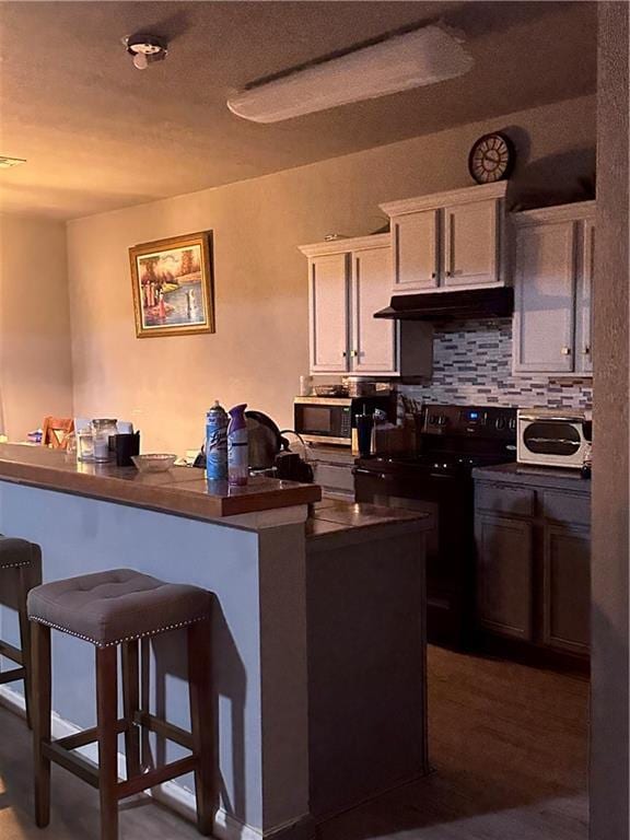 kitchen featuring a kitchen bar, backsplash, a textured ceiling, dark wood-type flooring, and electric stove