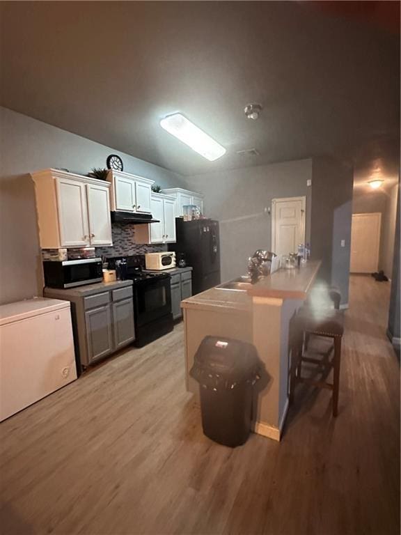 kitchen featuring tasteful backsplash, a breakfast bar, black appliances, light hardwood / wood-style flooring, and white cabinetry