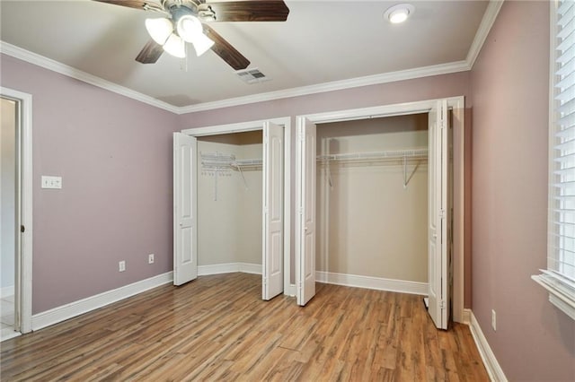 unfurnished bedroom featuring ceiling fan, light hardwood / wood-style floors, crown molding, and multiple closets