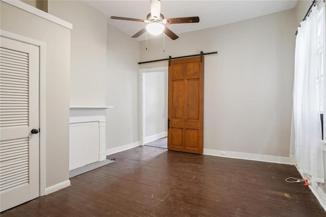 unfurnished bedroom featuring a closet, a barn door, dark hardwood / wood-style floors, and ceiling fan