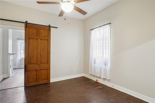 unfurnished room featuring a barn door, dark hardwood / wood-style floors, plenty of natural light, and ceiling fan