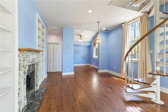 unfurnished living room featuring dark hardwood / wood-style floors, ceiling fan, a fireplace, and built in shelves