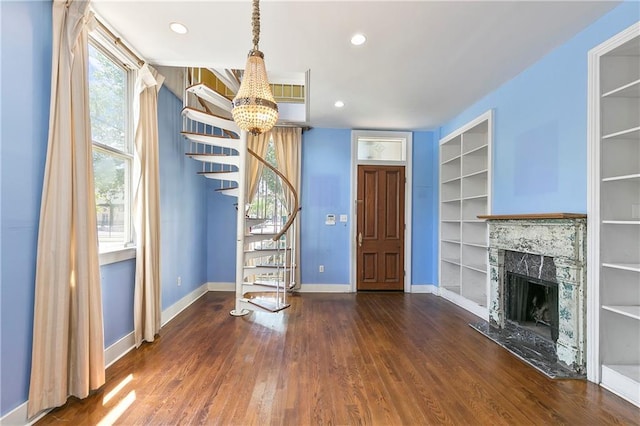 unfurnished living room with a high end fireplace, dark hardwood / wood-style flooring, built in features, and a notable chandelier