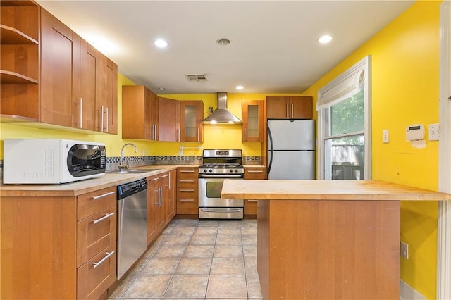 kitchen with stainless steel appliances, sink, wall chimney range hood, light tile patterned floors, and butcher block countertops