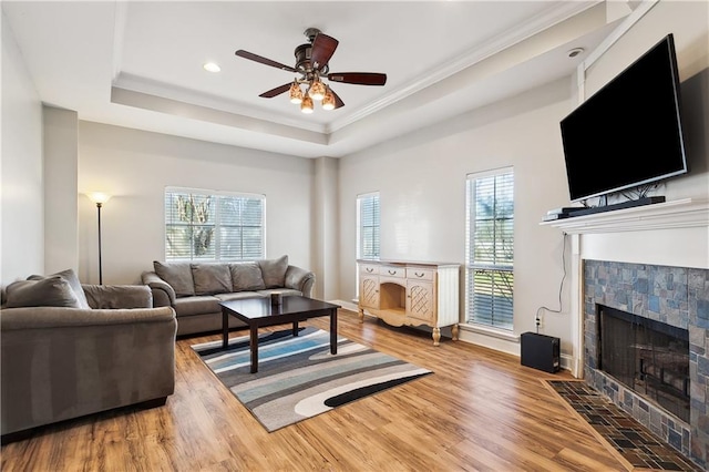 living room featuring a tile fireplace, hardwood / wood-style flooring, ceiling fan, and a tray ceiling