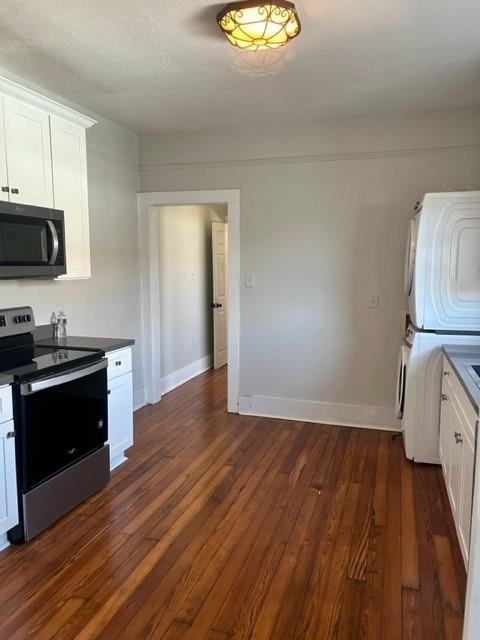 kitchen with dark hardwood / wood-style floors, stacked washing maching and dryer, a textured ceiling, white cabinetry, and stainless steel appliances