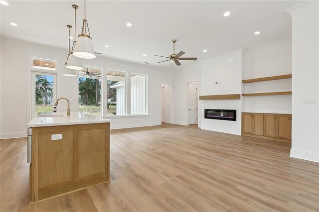 kitchen with sink, light hardwood / wood-style flooring, hanging light fixtures, an island with sink, and ornamental molding