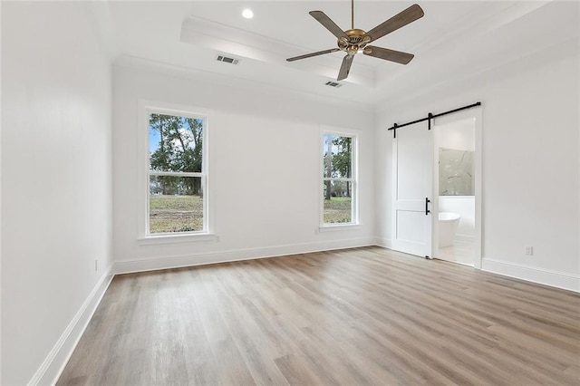 unfurnished bedroom featuring multiple windows, ensuite bathroom, ceiling fan, a tray ceiling, and a barn door