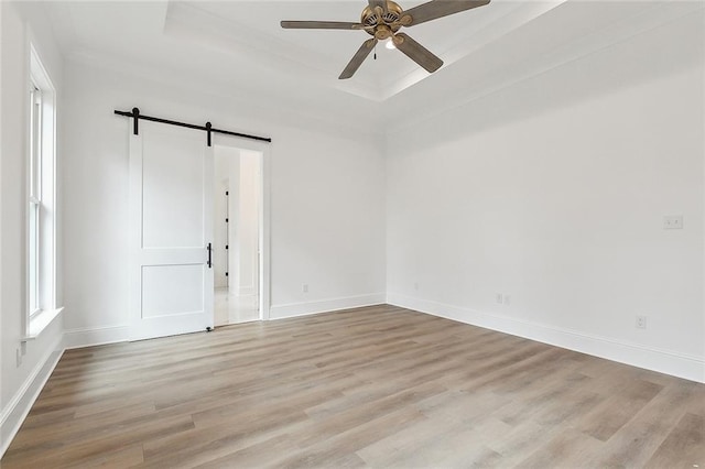 empty room with a raised ceiling, a barn door, ceiling fan, and light hardwood / wood-style floors