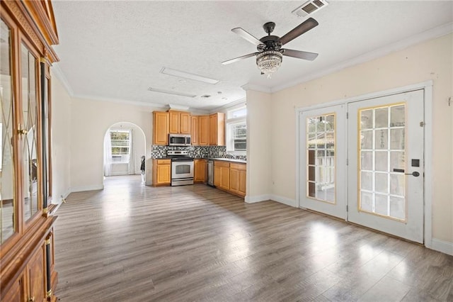 kitchen featuring appliances with stainless steel finishes, light wood-type flooring, backsplash, a textured ceiling, and crown molding