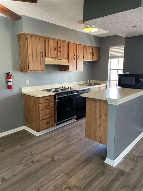 kitchen featuring black appliances, sink, dark hardwood / wood-style floors, a textured ceiling, and kitchen peninsula