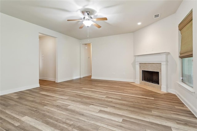 unfurnished living room with light hardwood / wood-style floors, ceiling fan, and a tiled fireplace