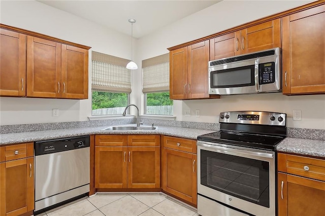 kitchen featuring sink, hanging light fixtures, light stone counters, light tile patterned floors, and appliances with stainless steel finishes