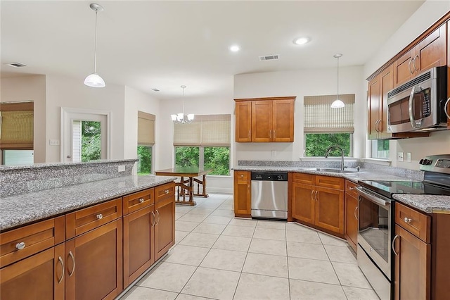 kitchen featuring sink, hanging light fixtures, plenty of natural light, light stone counters, and stainless steel appliances