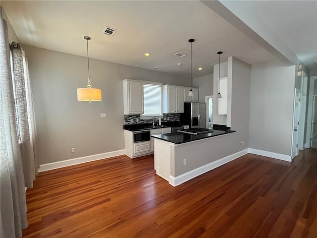 kitchen featuring pendant lighting, dark wood-type flooring, tasteful backsplash, white cabinetry, and stainless steel appliances