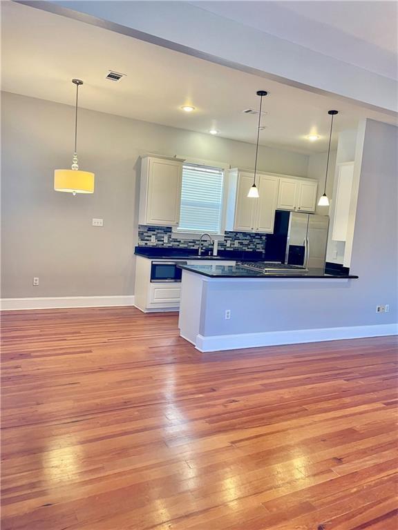 kitchen featuring hanging light fixtures, light hardwood / wood-style flooring, white cabinets, and stainless steel appliances