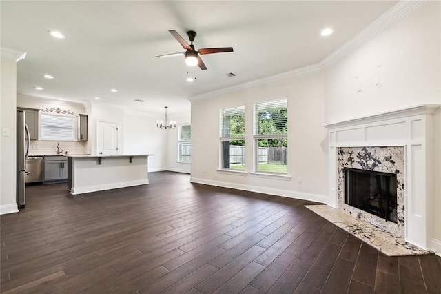 unfurnished living room featuring ceiling fan with notable chandelier, ornamental molding, a fireplace, and dark wood-type flooring