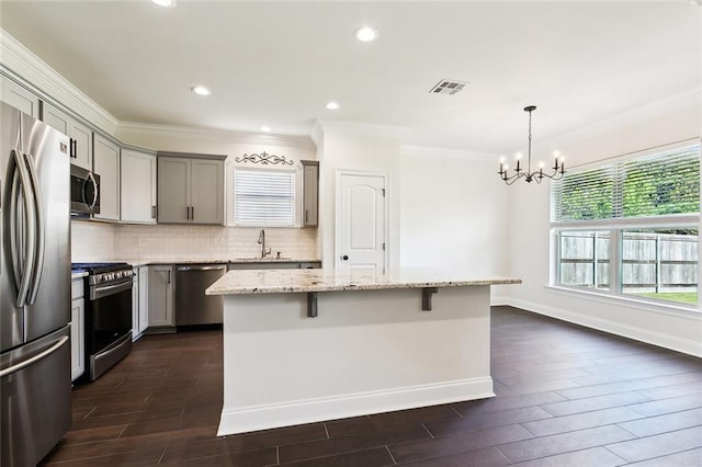 kitchen featuring appliances with stainless steel finishes, light stone counters, gray cabinetry, pendant lighting, and a center island