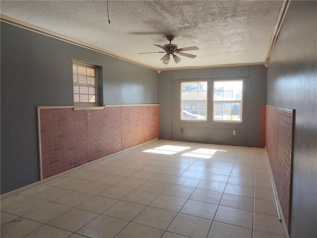 tiled spare room with ceiling fan, ornamental molding, a textured ceiling, and brick wall