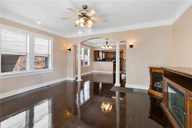 living room with ornate columns, crown molding, dark wood-type flooring, and ceiling fan with notable chandelier