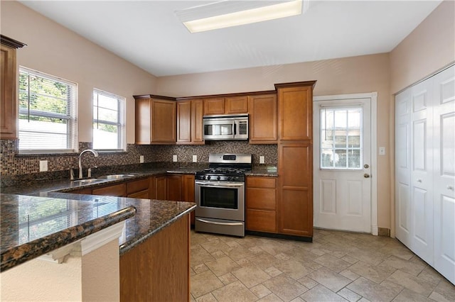 kitchen with appliances with stainless steel finishes, tasteful backsplash, dark stone countertops, and sink