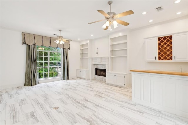 unfurnished living room with a fireplace, built in features, and ceiling fan