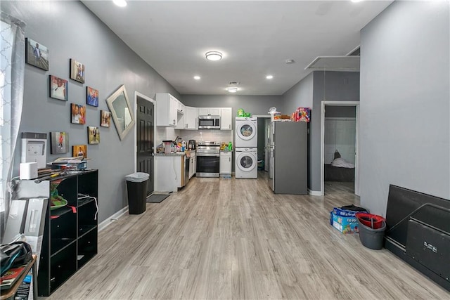 kitchen with stacked washing maching and dryer, stainless steel appliances, light hardwood / wood-style flooring, decorative backsplash, and white cabinets