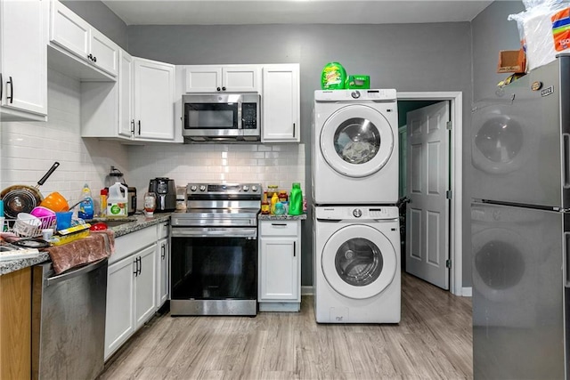 kitchen with white cabinets, light hardwood / wood-style floors, stacked washer / drying machine, and appliances with stainless steel finishes