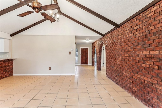 spare room featuring light tile patterned floors, ceiling fan, a textured ceiling, brick wall, and beamed ceiling