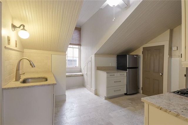 kitchen featuring ceiling fan, sink, light stone counters, stainless steel fridge, and white cabinets