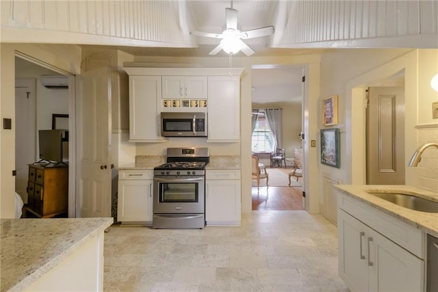 kitchen featuring an AC wall unit, sink, light stone countertops, appliances with stainless steel finishes, and white cabinetry