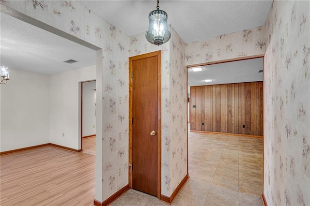 hall featuring wood walls, light hardwood / wood-style floors, and a textured ceiling