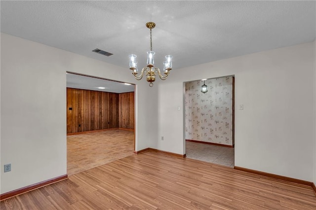 empty room with wood walls, a chandelier, a textured ceiling, and light wood-type flooring