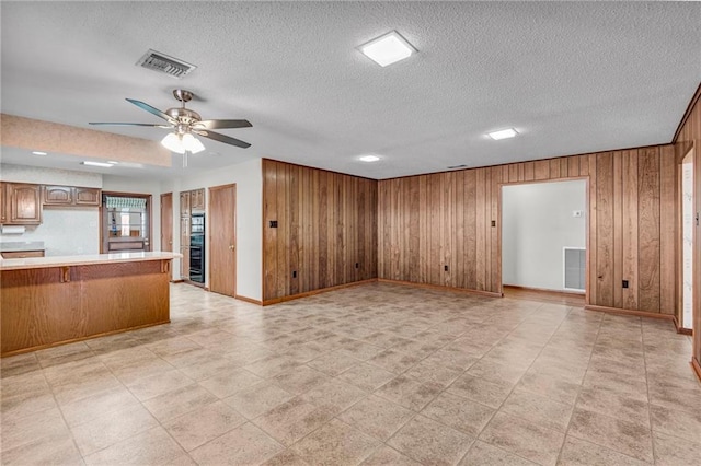 unfurnished living room featuring a textured ceiling, ceiling fan, and wooden walls