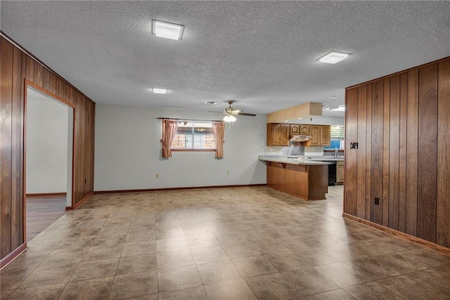 kitchen featuring ceiling fan, sink, kitchen peninsula, wood walls, and a textured ceiling