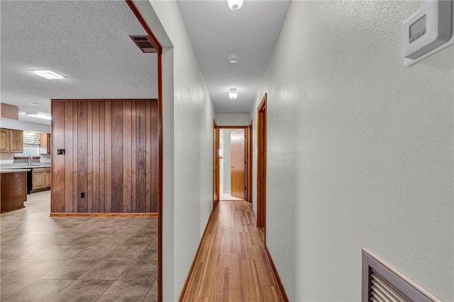 hallway featuring sink, a textured ceiling, and light hardwood / wood-style flooring