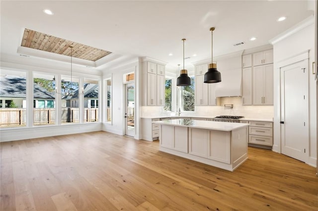 kitchen with white cabinetry, pendant lighting, a raised ceiling, and a kitchen island