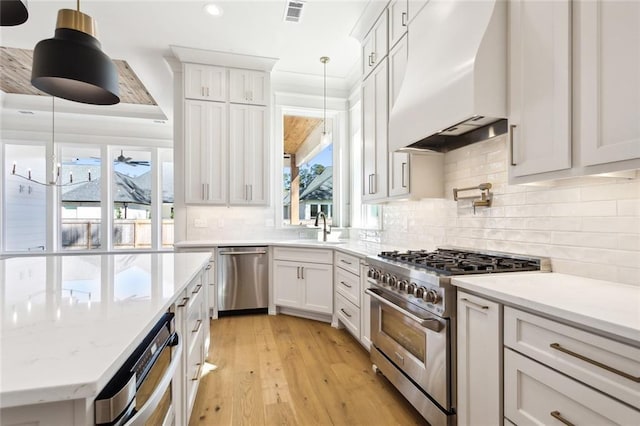 kitchen featuring appliances with stainless steel finishes, decorative light fixtures, sink, white cabinets, and custom range hood