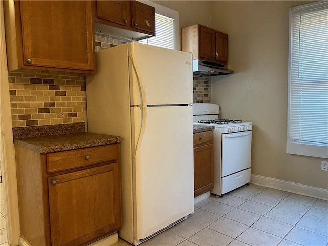 kitchen with white appliances, baseboards, light tile patterned flooring, under cabinet range hood, and dark countertops